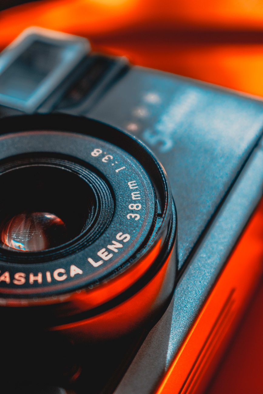 Capture of a vintage camera lens highlighting its details against a vibrant orange background.