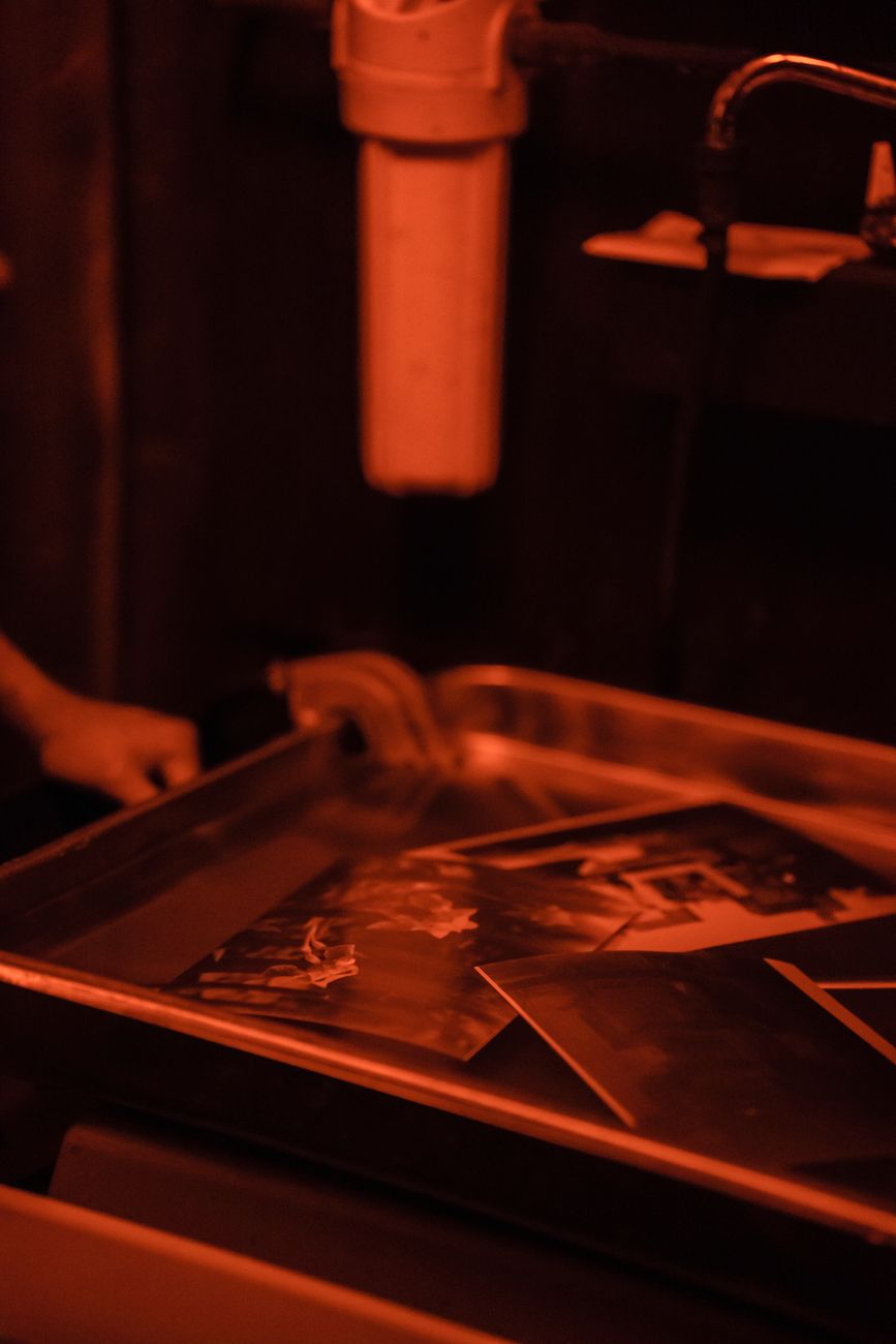 Close-up of photographs being developed in a darkroom under red lighting.