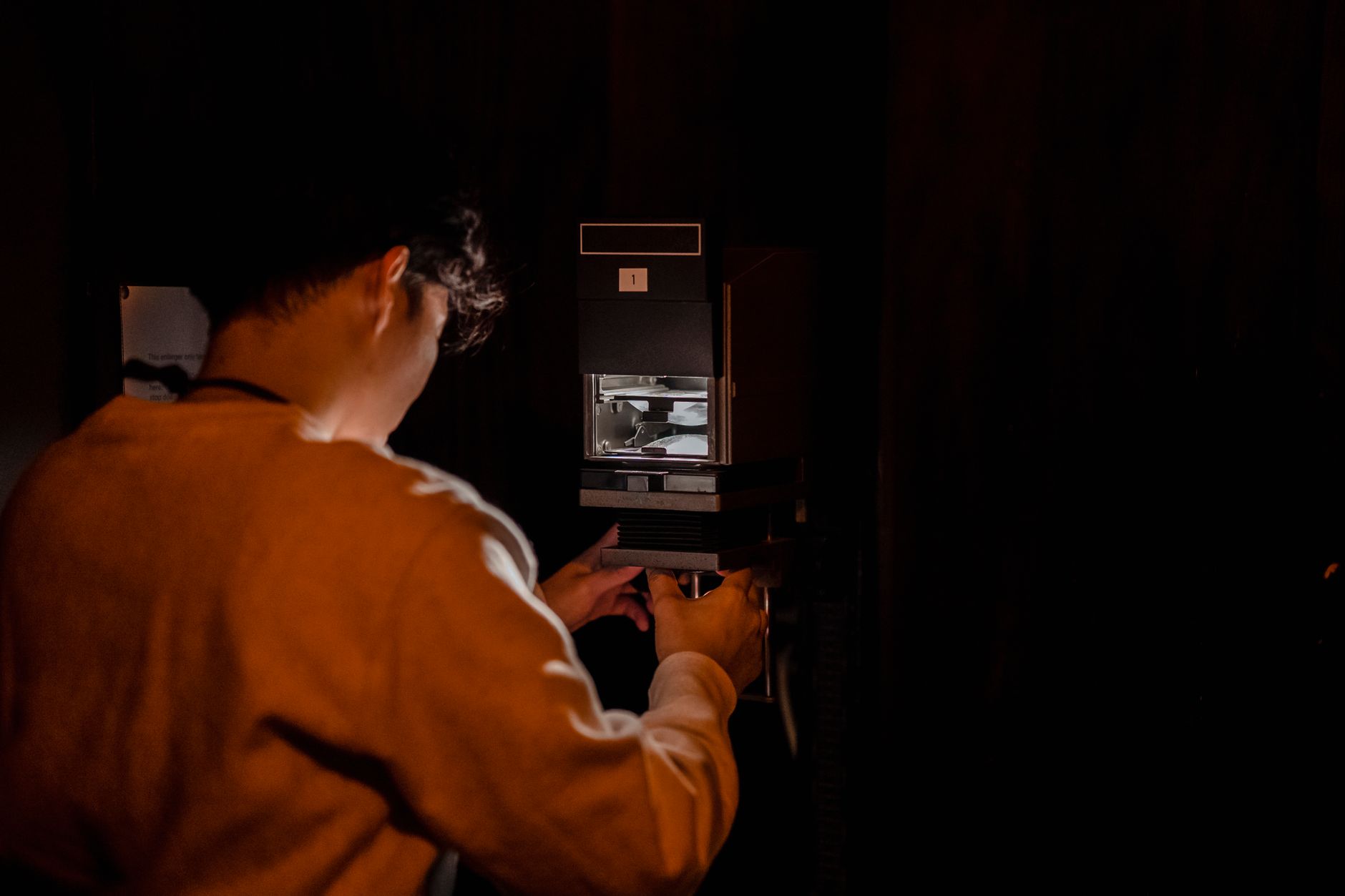 A photographer processes film in a darkroom under red lighting, using analogue techniques.