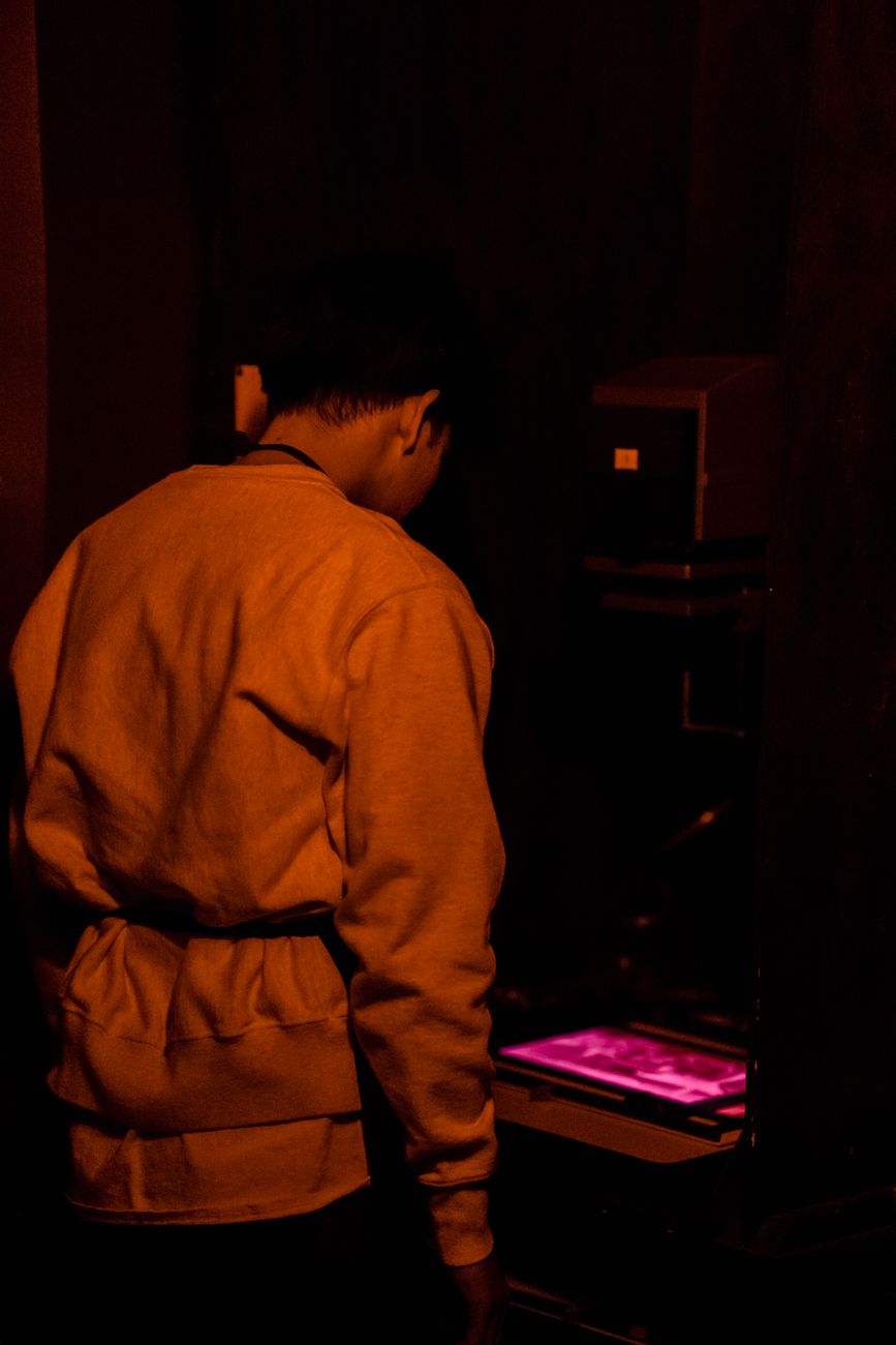 An adult in a darkroom developing photographic prints under red light.